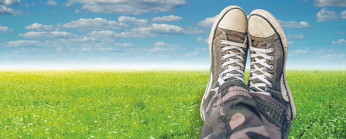 image of someone crossing their feet in a meadow with clouds in the sky